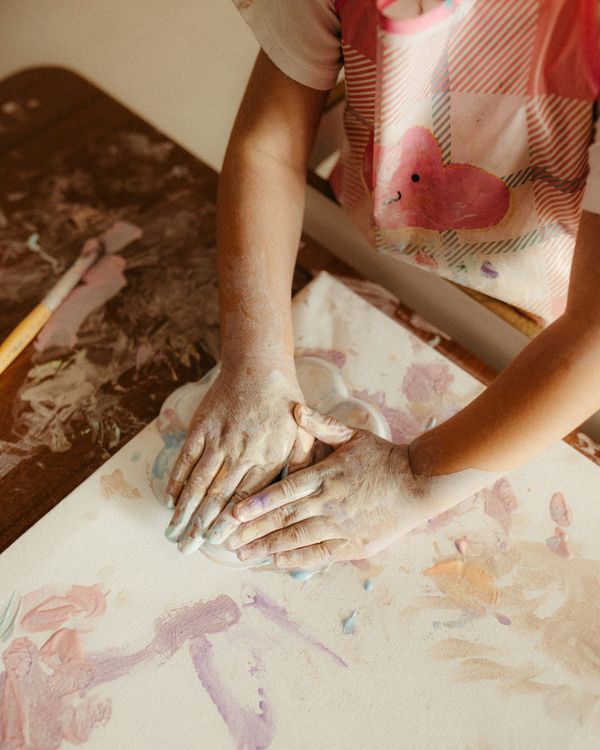 A child's paint-covered hands working on a colourful painting
