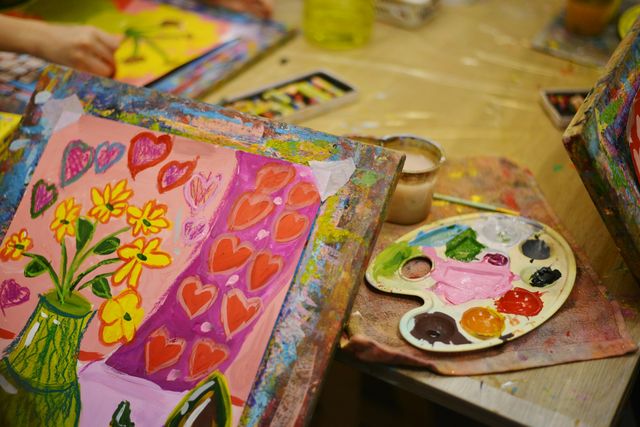 A table covered in paints, brushes and palettes in an art room