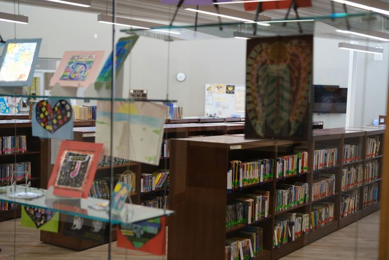 Children's artwork displayed on glass panels beside library bookshelves